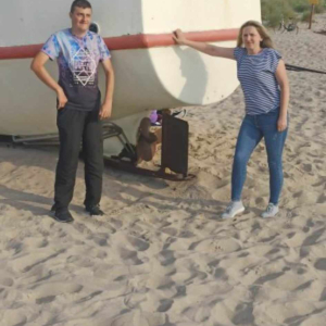 na zdjęciu widać łódź zacumowaną na plaży, przy której stoją dwie osoby